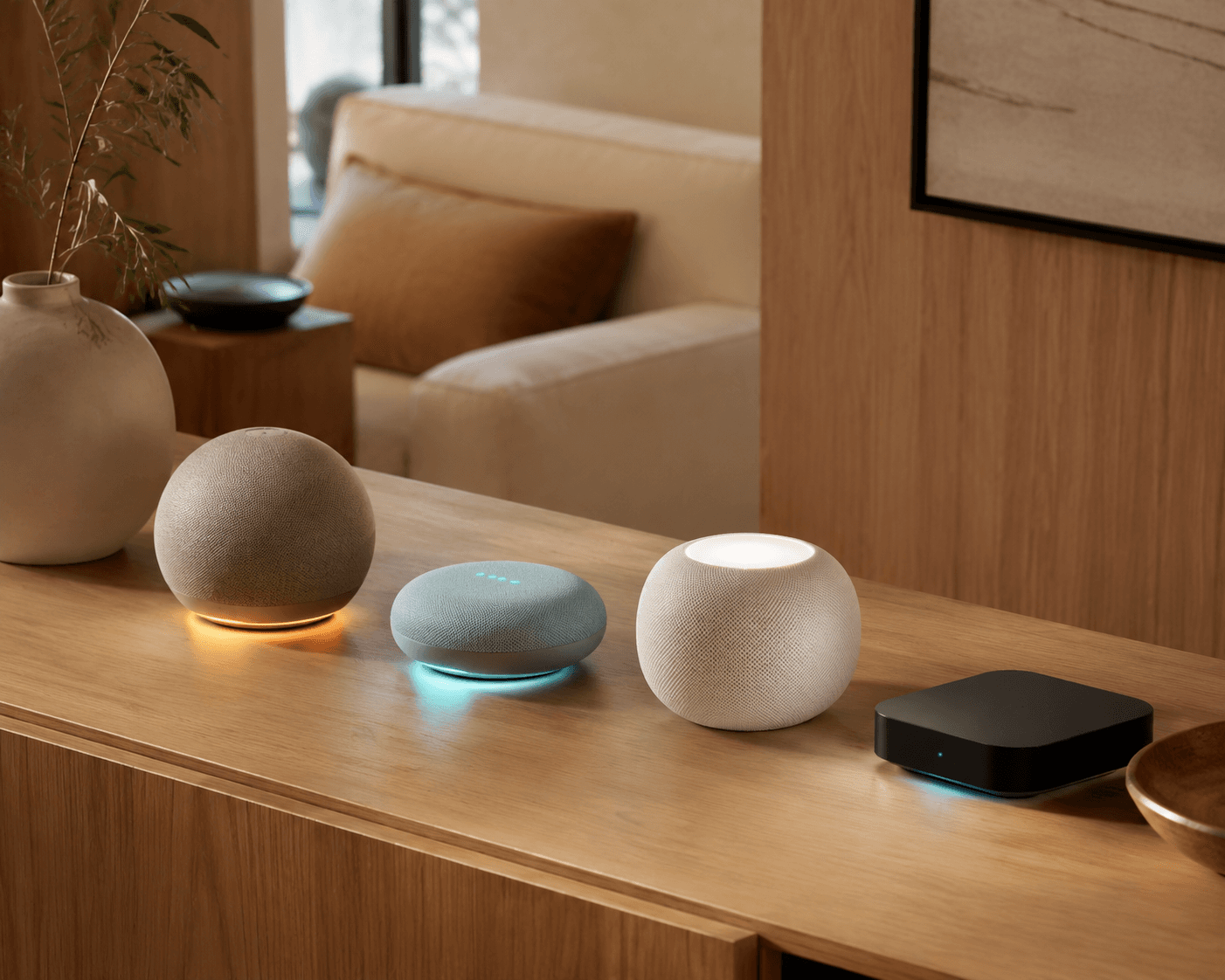 Four smart home hub devices arranged on a console table in a modern living room