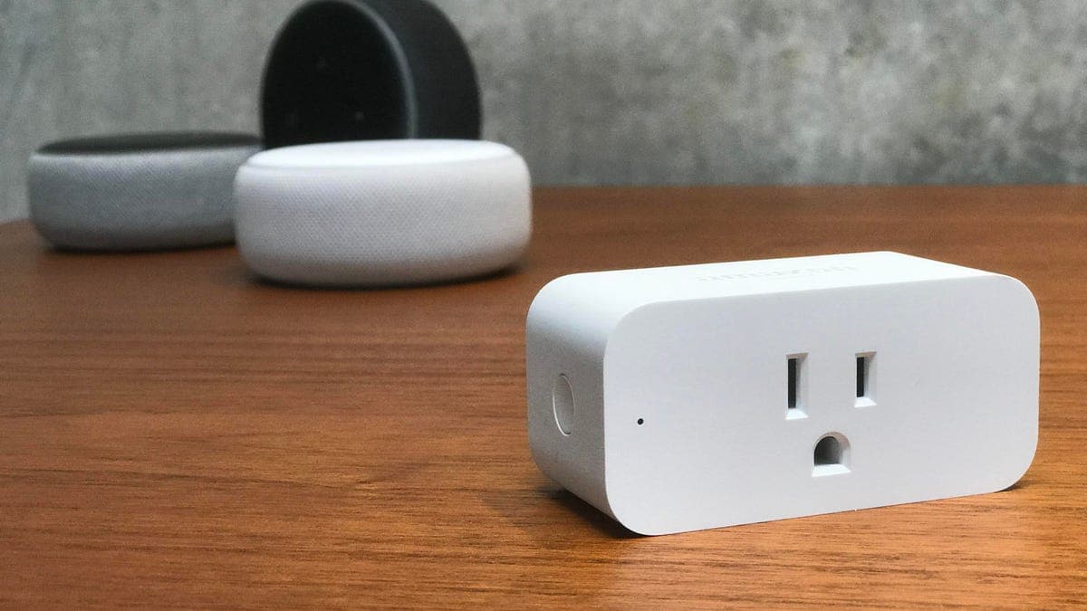 Amazon Smart Plug next to a white Echo Dot, showing the front-facing outlet and blue LED indicator