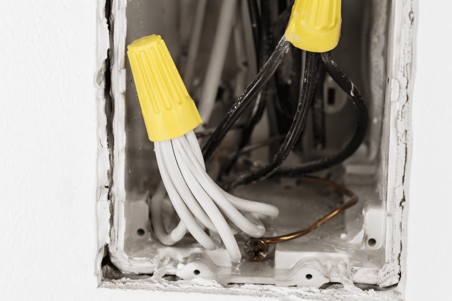 Close-up of an open switch box with white neutral wires capped together, black hot wires, and a bare copper ground wire
