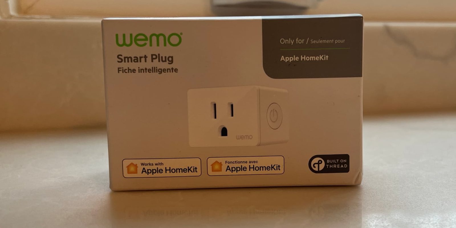 A compact white Wemo Smart Plug with Thread on a dark wooden surface