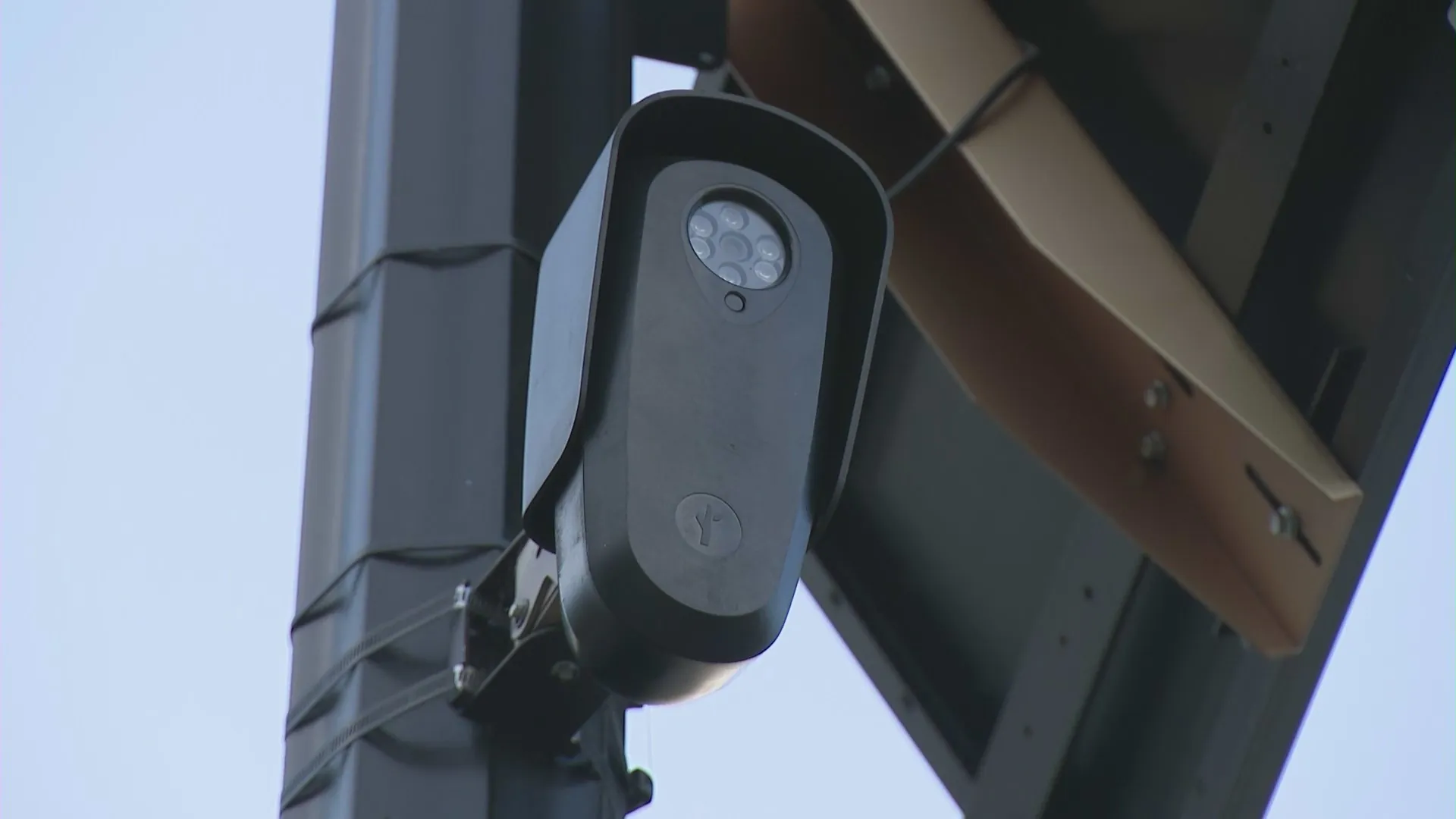 Flock Safety automated license plate reader camera mounted on a street pole in a residential neighborhood with a police vehicle nearby